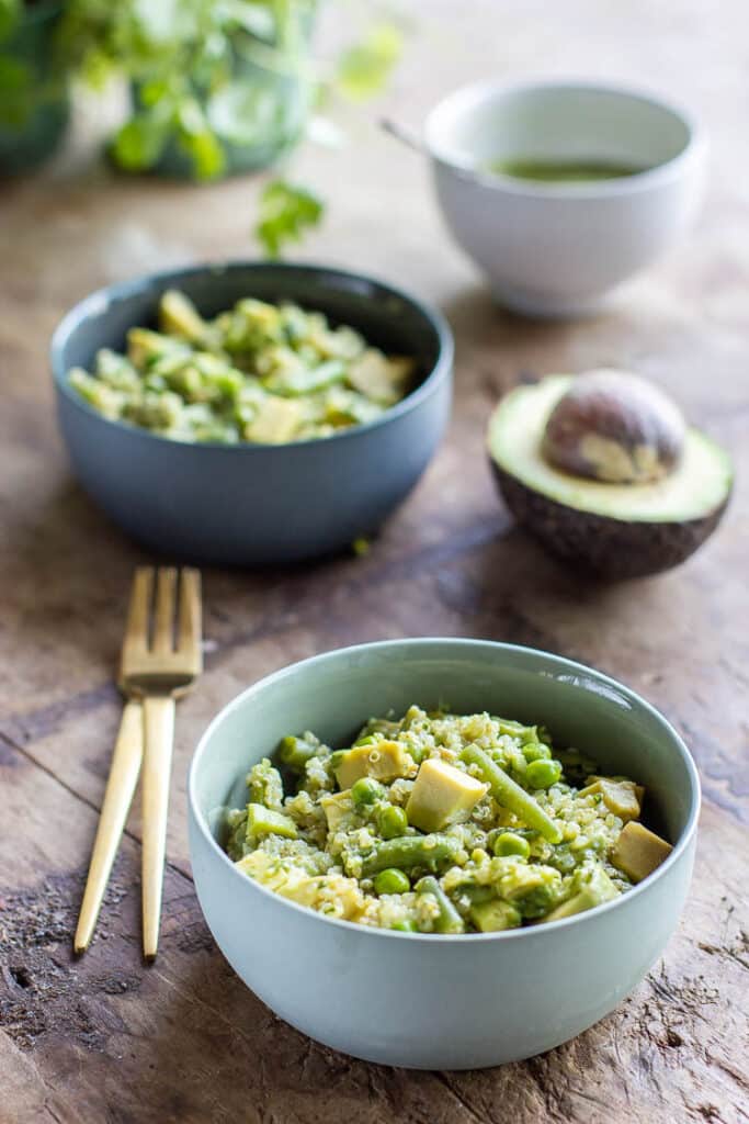 Bols de salade de quinoa, cubes d'avocat, haricots verts, petits pois et bol de sauce verte à base de fines herbes et avocat.